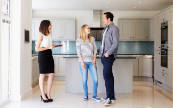 A man and woman in a kitchen with a realtor during a tour of a house; keeping their budget in mind after receiving preapproval from a mortgage lender.