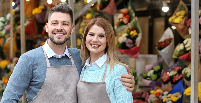 Couple business owners posing in front of floral shop with matching aprons on.